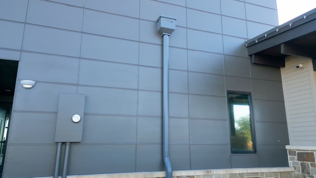 Gray building exterior featuring a utility box, water pipe, and window. Modern architectural design.
