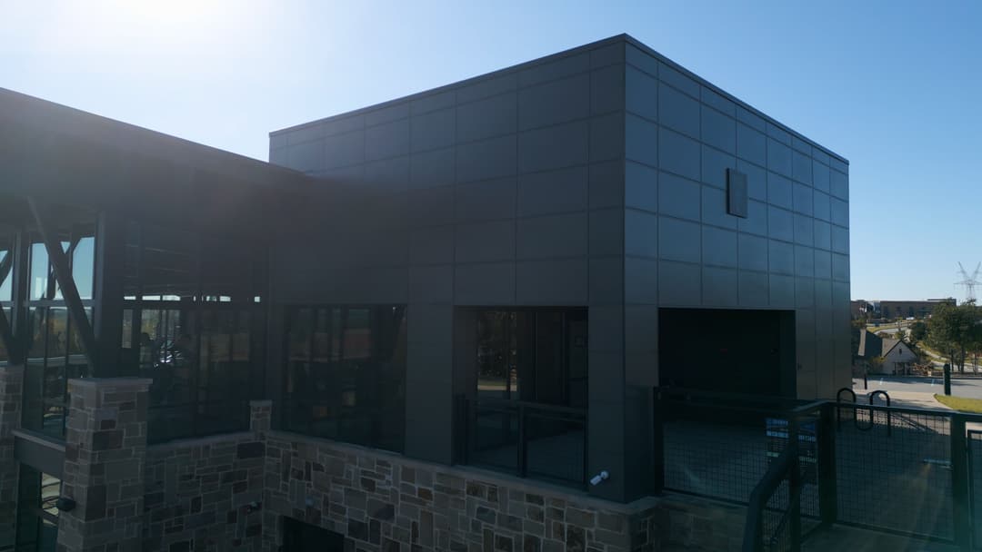 Modern building exterior with sleek black panels and large windows under clear blue sky.