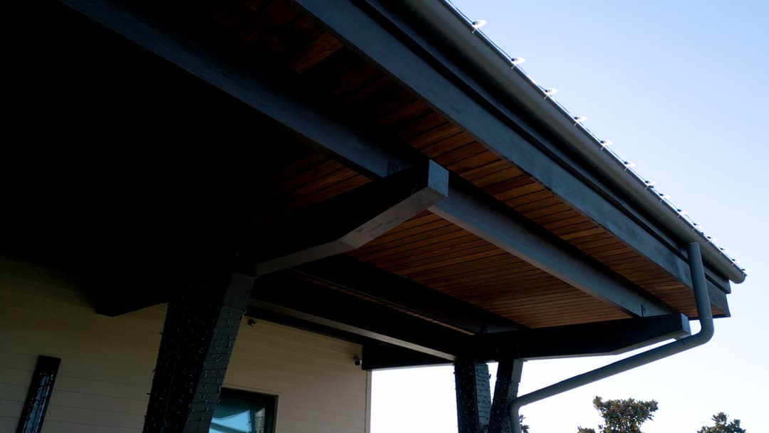 Modern black patio with wooden ceiling and metal support beams against clear blue sky.