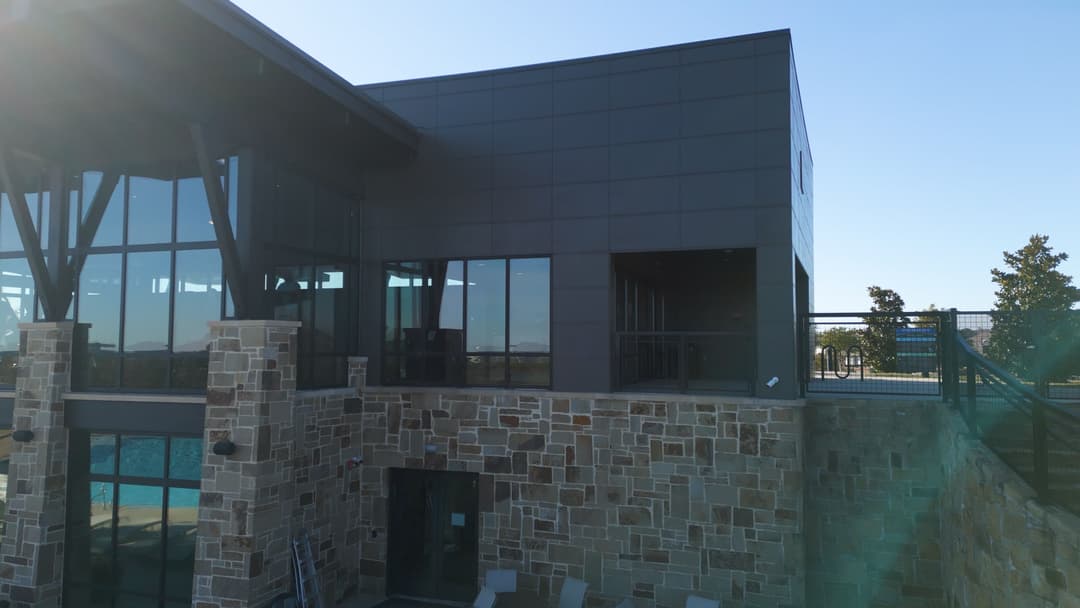 Modern building exterior featuring stone accents and large glass windows against a blue sky.