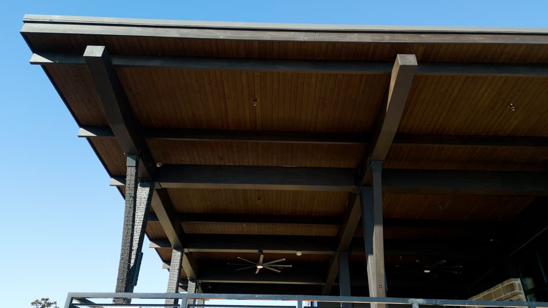 Modern architecture featuring wooden beams and a spacious overhang against a clear blue sky.