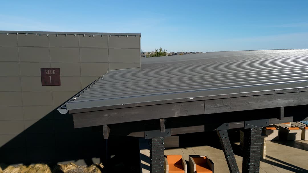 Modern building with a sleek metal roof under a clear blue sky. BLDG 1 sign visible.