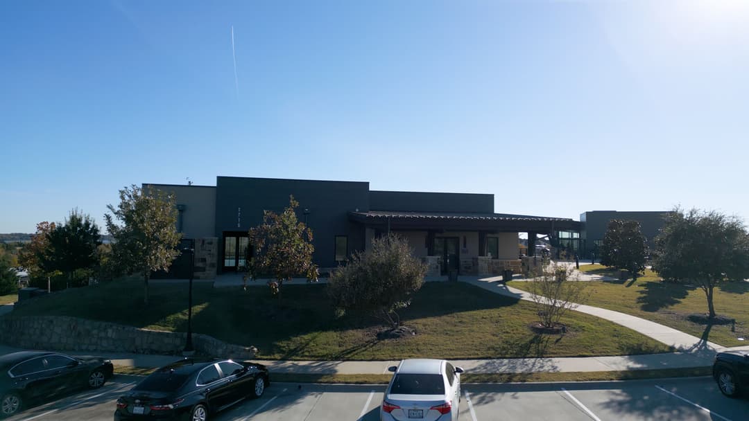 Modern commercial building with landscaped entrance and parked cars under clear blue sky.