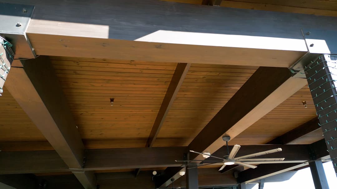 Wooden ceiling beams with ceiling fan and holiday lights, creating a warm outdoor atmosphere.