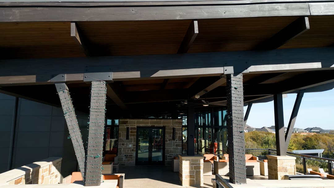 Modern building entrance with wooden beams, stone accents, and outdoor seating area.