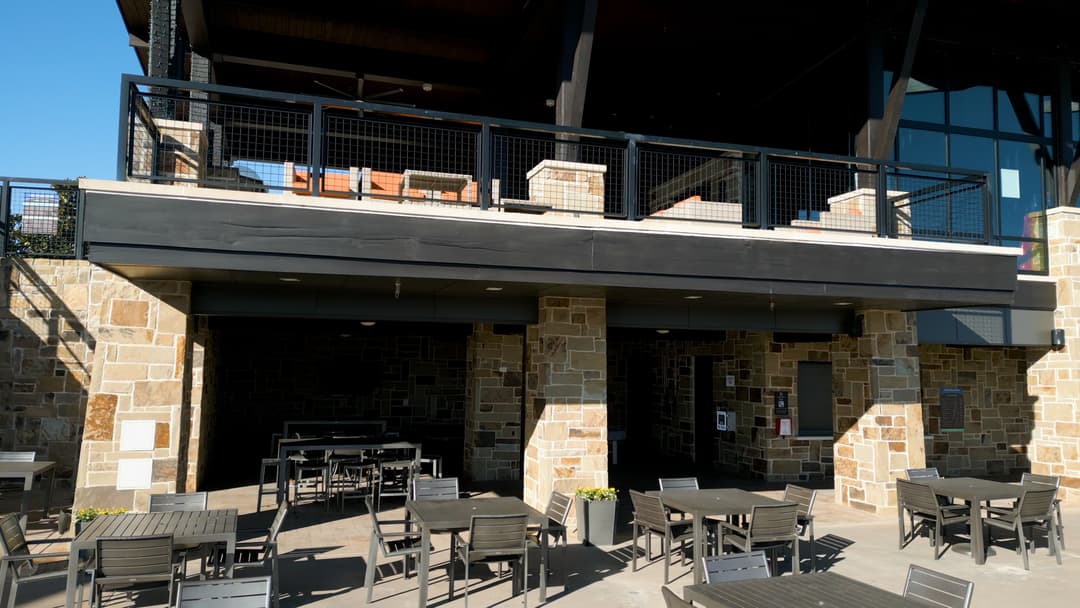 Outdoor dining area with stone architecture and modern tables under a large building.