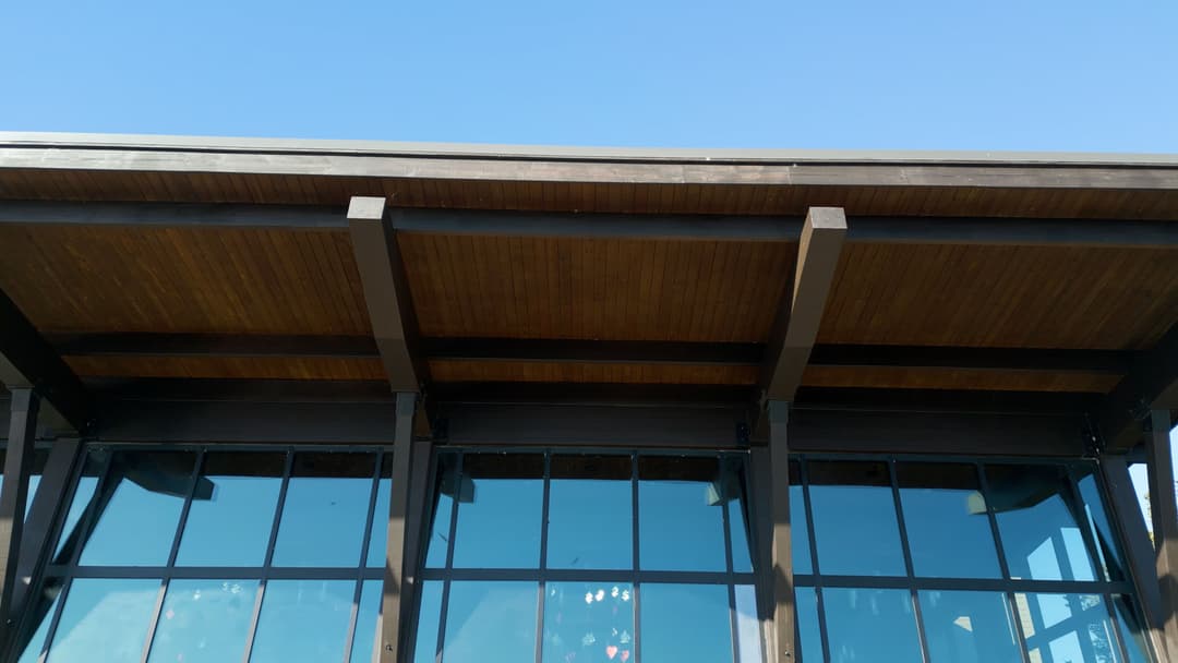 Modern building exterior with wooden roof beams and large glass windows against a clear blue sky.