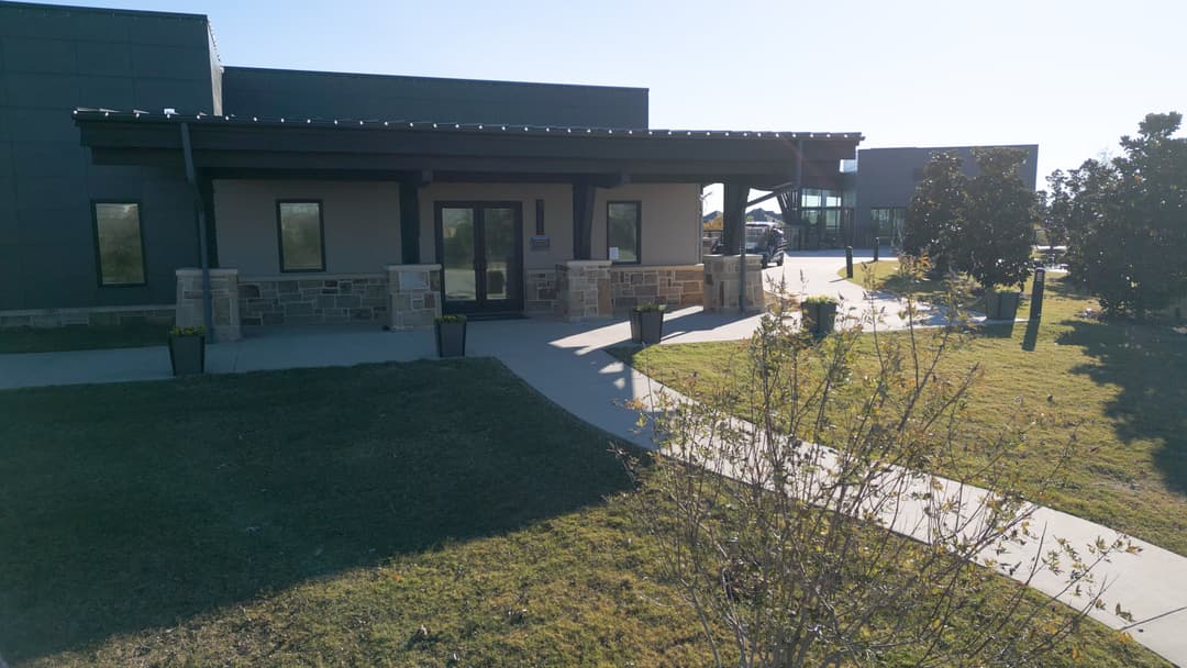Modern building entrance with stone accents and landscaped pathway under clear blue sky.