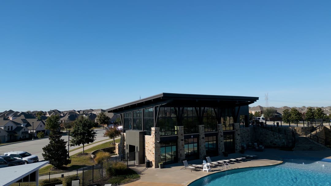Modern leisure center with a pool against a clear blue sky and suburban backdrop.
