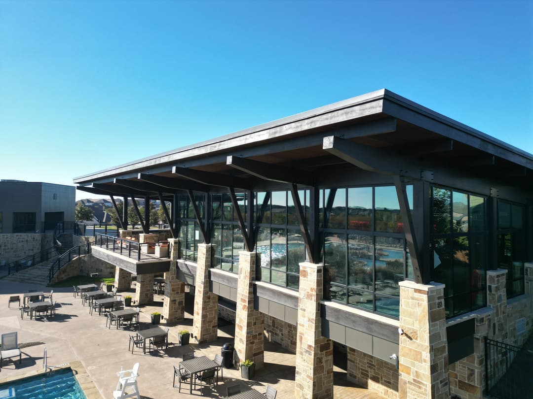 Modern building with large windows overlooking a pool area under a clear blue sky.