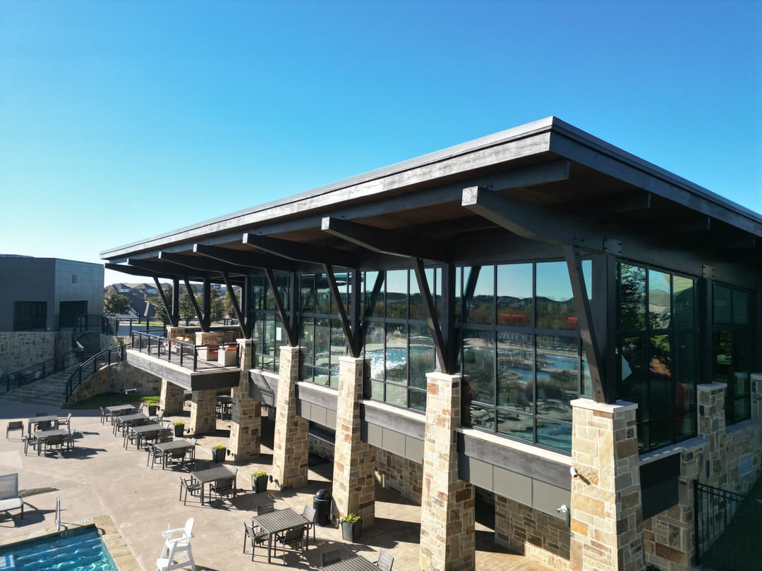 Modern architectural building with large windows and stone accents overlooking a pool area.