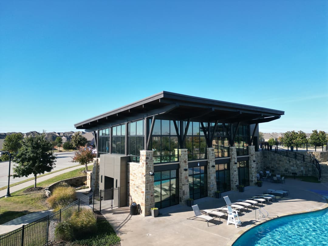 Modern poolside clubhouse with large windows, seating area, and clear blue sky.