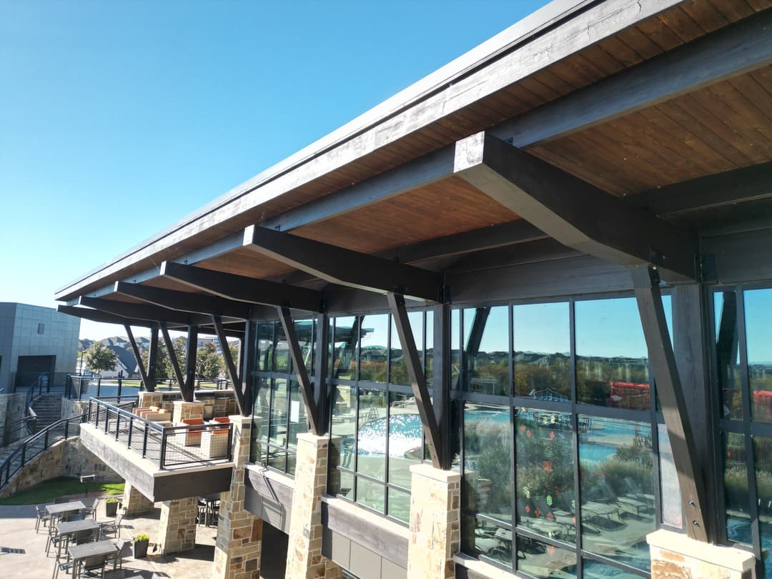 Modern building exterior with large glass windows and wooden beams against a clear blue sky.