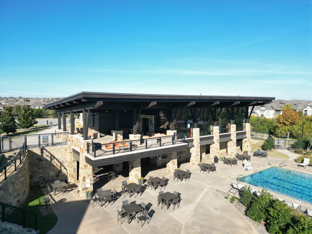 Contemporary poolside clubhouse with outdoor seating and clear blue sky background.