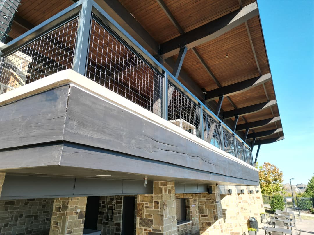 Modern building exterior featuring a wooden balcony with metal railing and stone foundation.