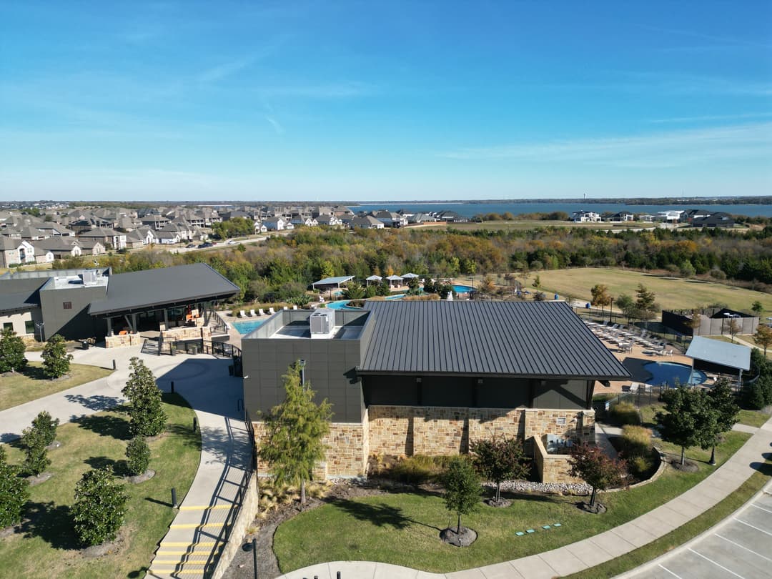 Aerial view of a modern facility with a pool, surrounded by greenery and homes.